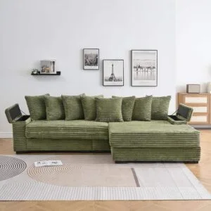 A comfortable green corduroy L-shaped sectional sofa with multiple plush cushions sits on a patterned rug in a bright living room. The sofa features visible hidden storage compartments and a built-in cup holder, showcasing its functional and stylish design within a modern home setting.